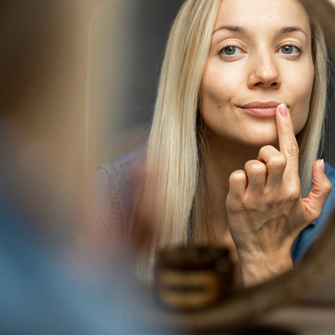 1. Woman applying HOIA homespa organic lip scrub in front of mirror, showcasing lip care routine