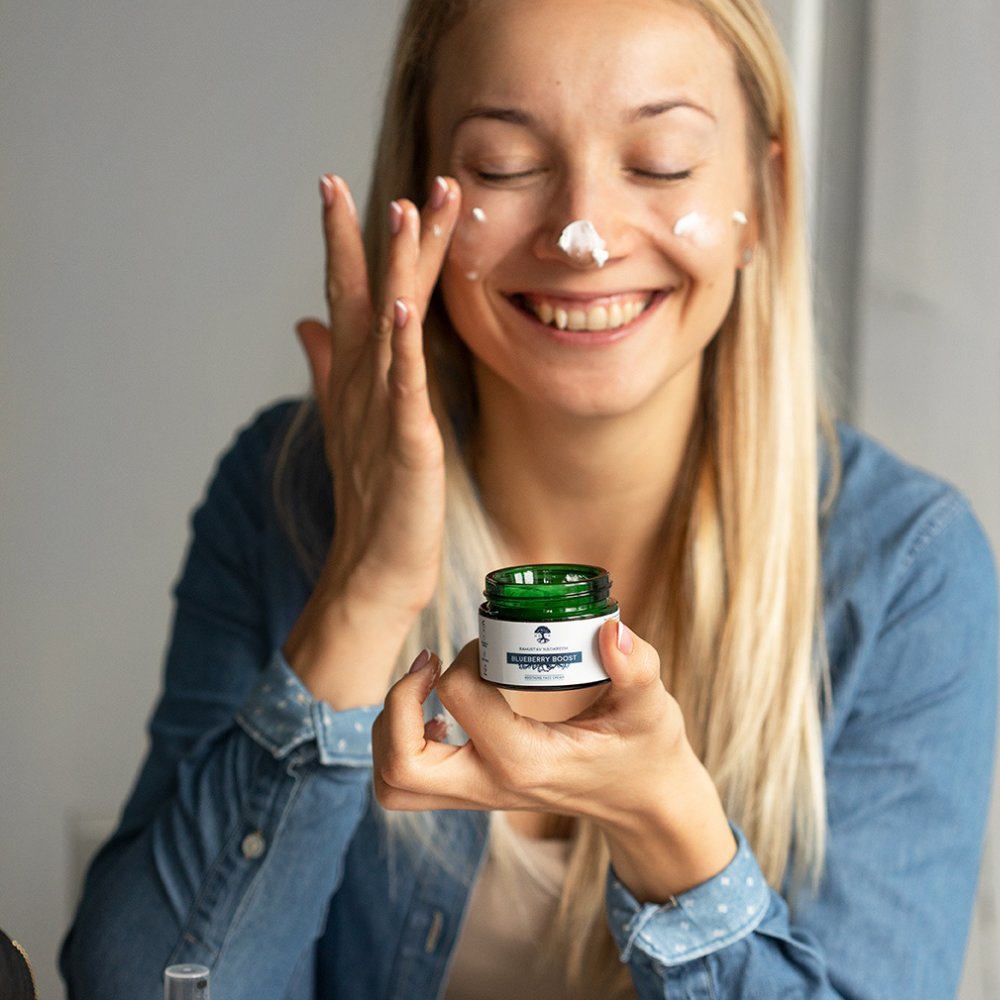 1. Woman applying HOIA homespa Soothing Face Cream Blueberry Boost, smiling in a lifestyle setting