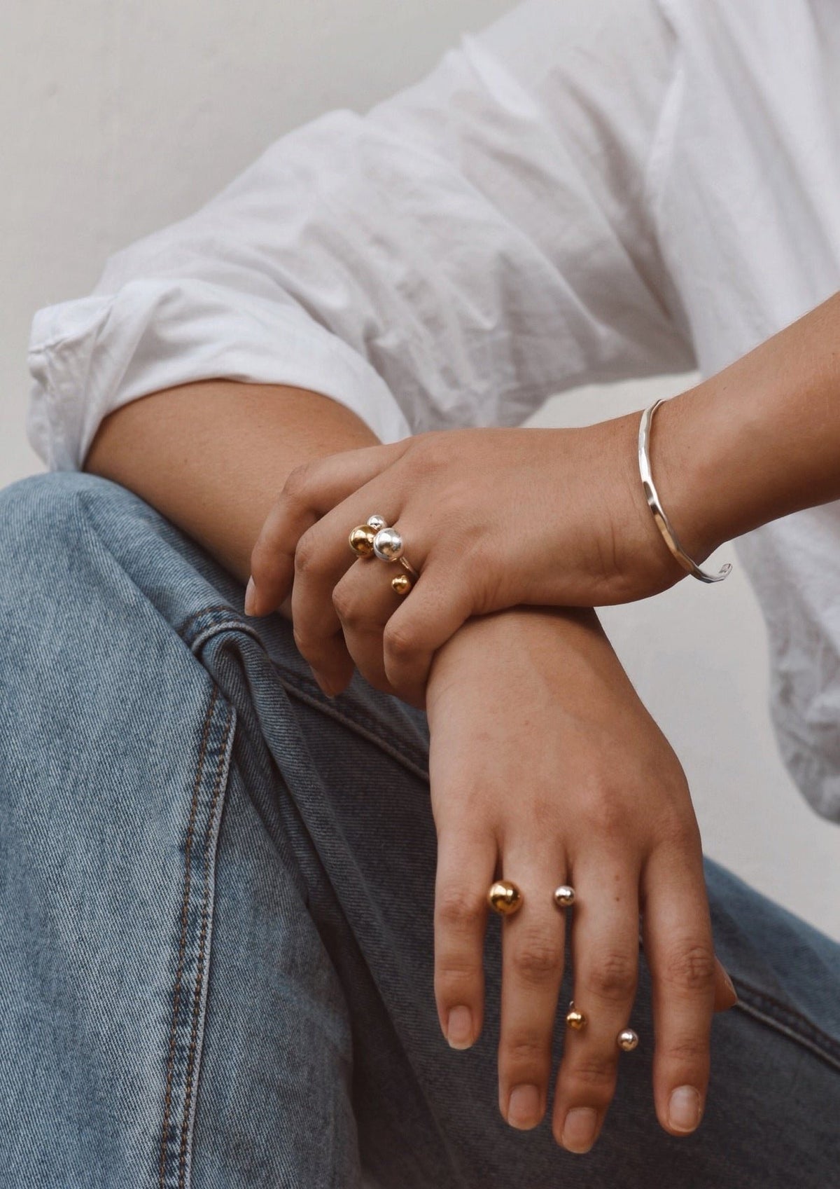 8. Woman wearing multiple NO MORE rings including Big Bomb Multisize Ring in gold, styled with a white shirt and jeans