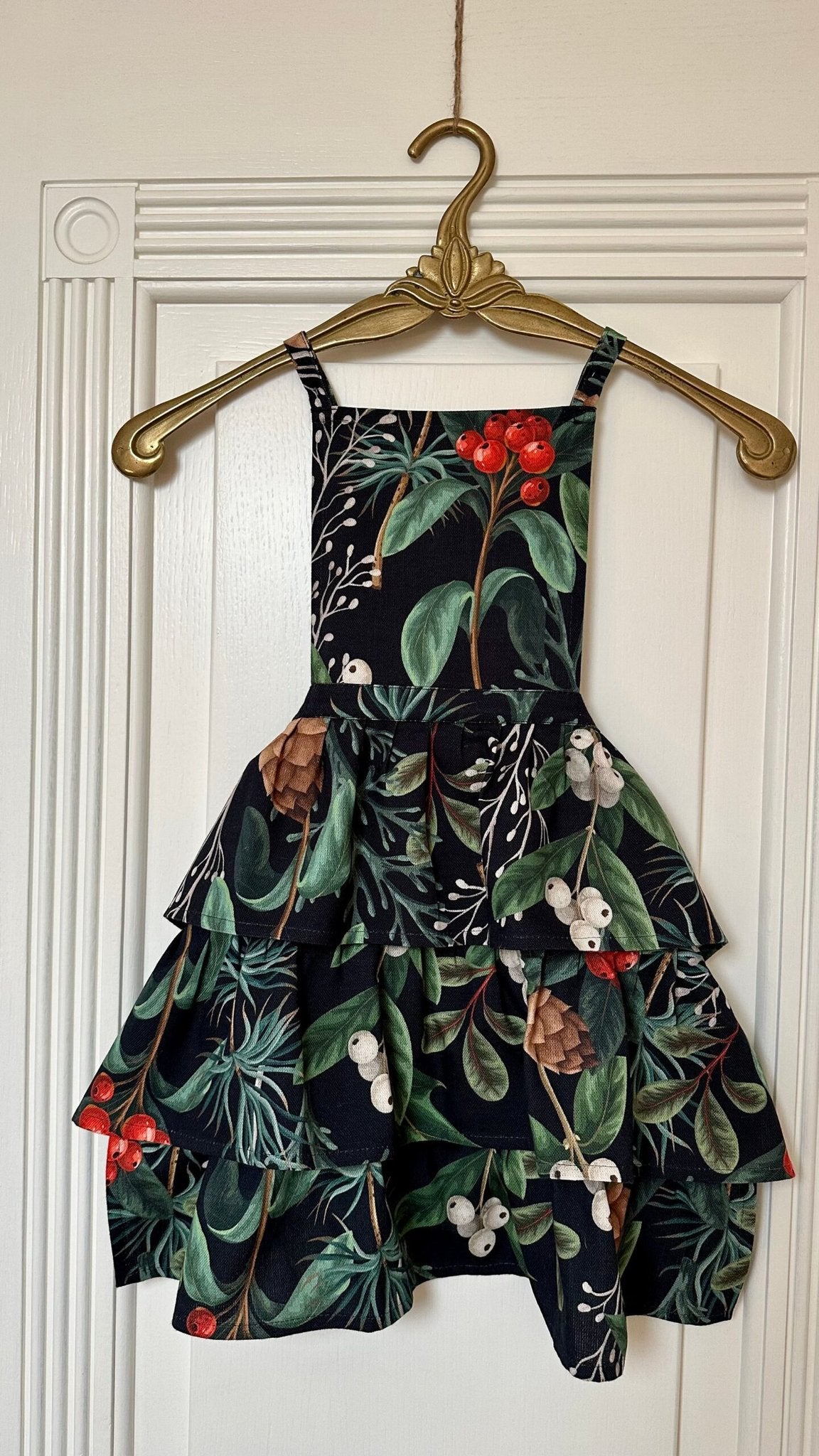 1. Kids apron with winter forest design by Hortensias Home, featuring pinecones and berries, shown on a hanger
