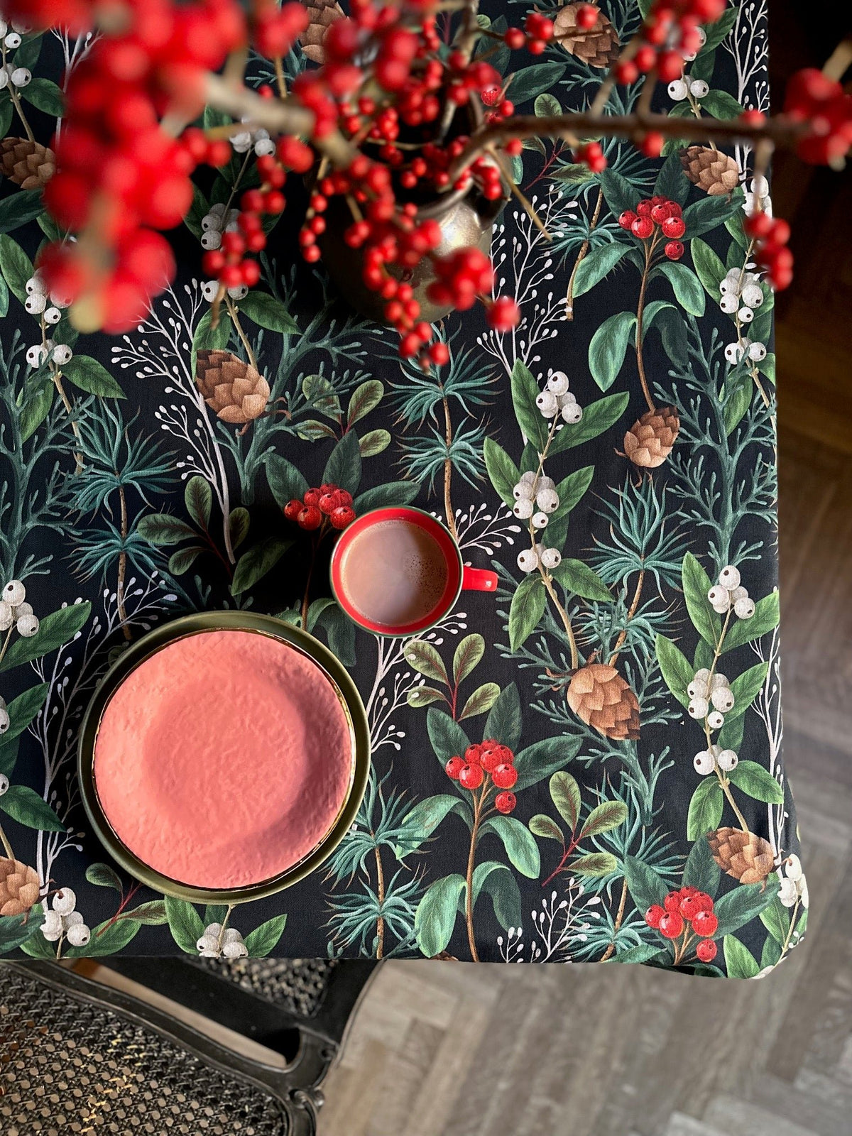 2. Hortensias Home Christmas Forest tablecloth with festive red berries and pinecones, shown with a red mug and pink plate for a holiday setting