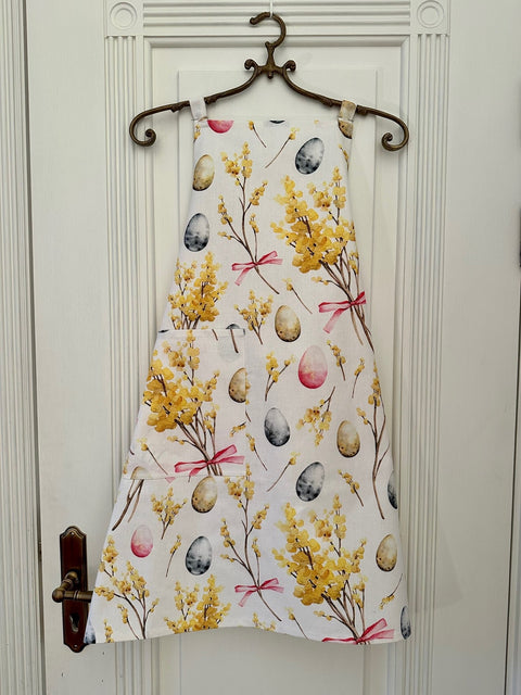 1. Women's Easter-themed apron by Hortensias Home featuring yellow floral and egg print, displayed on a hanger