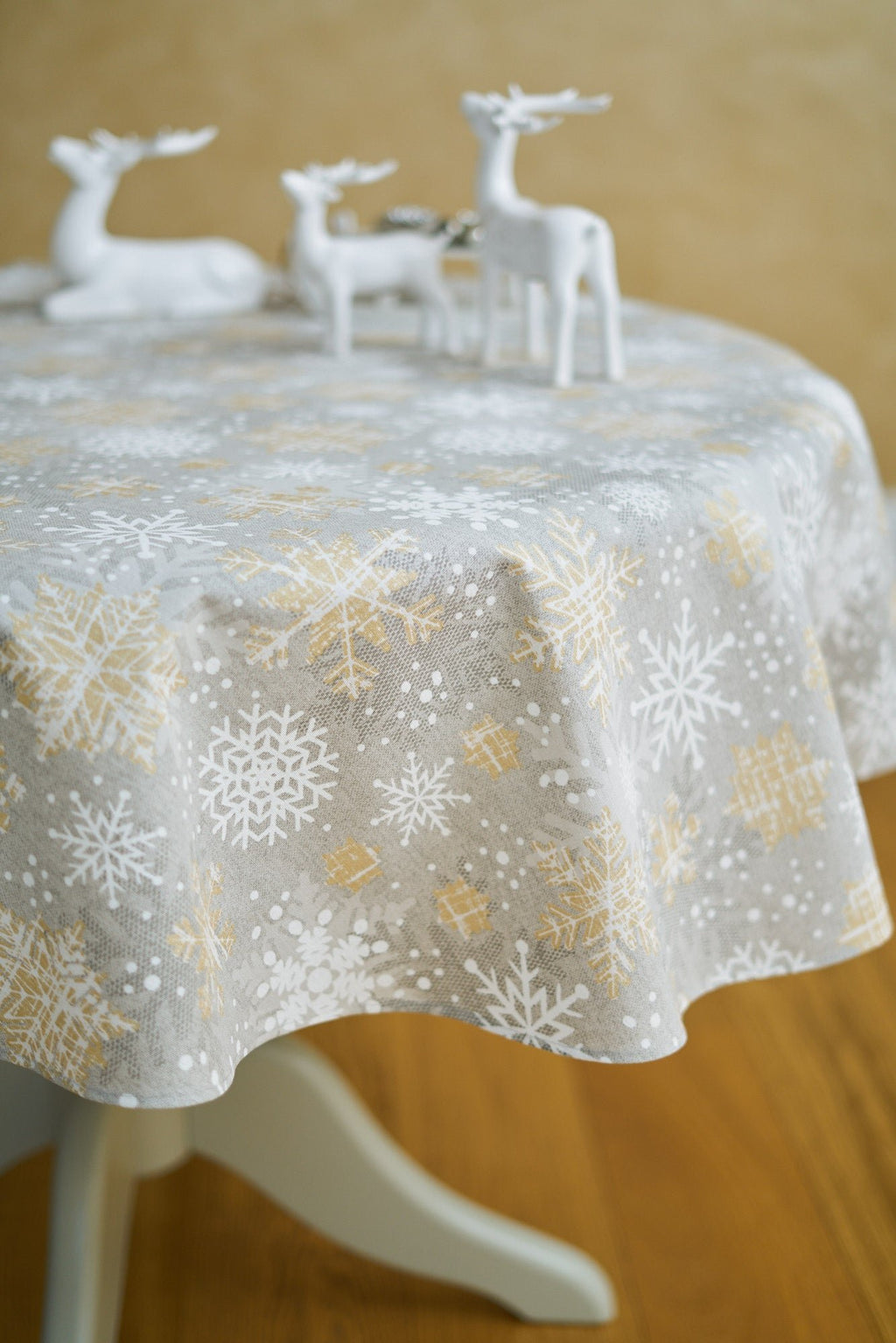 1. Hortensias Home Christmas snowflake tablecloth in gold and grey, styled with decorative reindeer on a round table