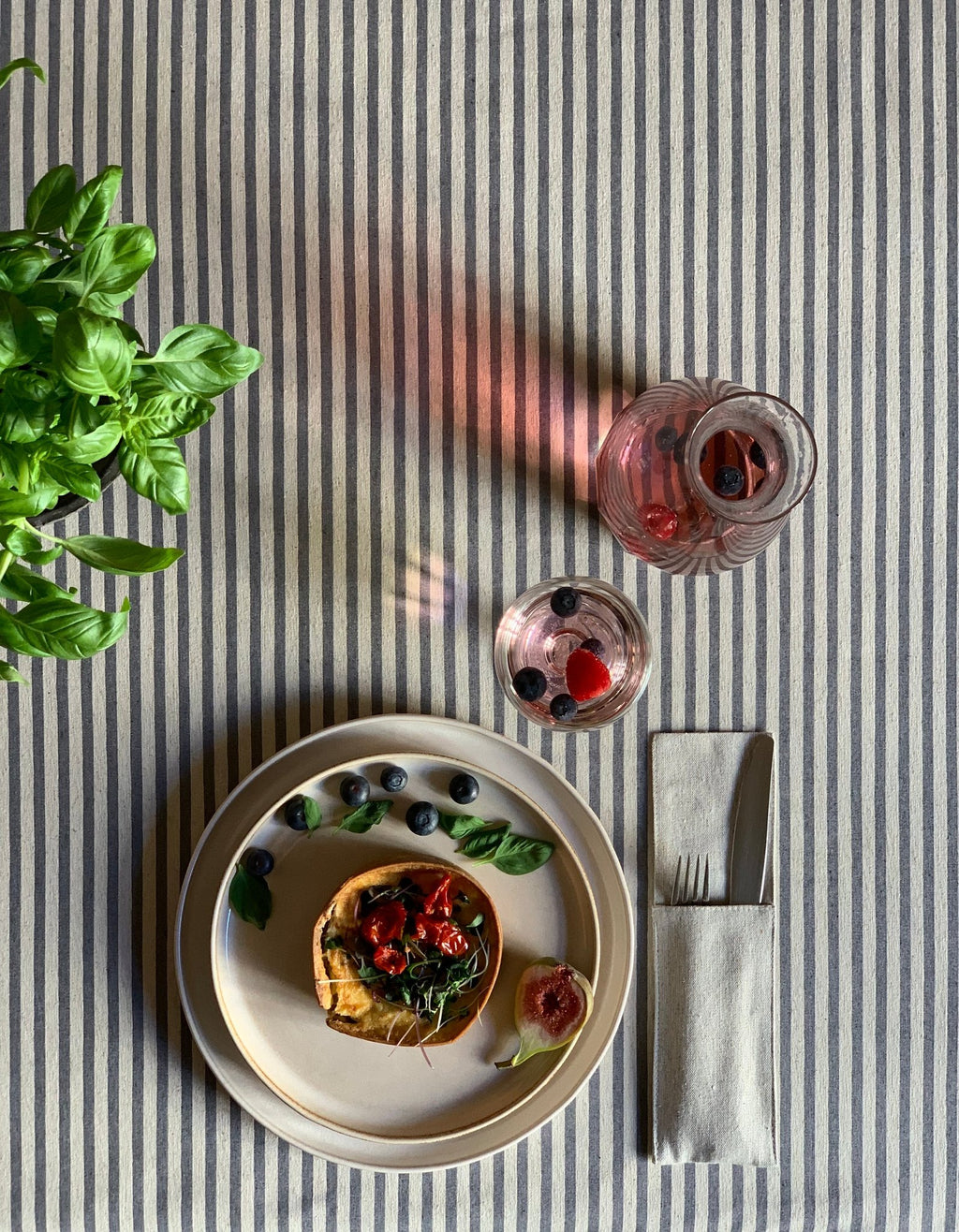 1. Rectangular tablecloth from Nord 1 Collection by Hortensias Home, featuring blue stripes, styled with a meal setting and plant, showcasing eco-friendly design