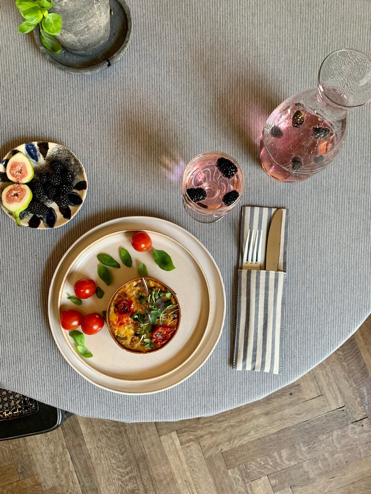 1. Lifestyle image of Nord 2 round tablecloth by Hortensias Home with subtle blue lines on beige, set with a meal and drinks