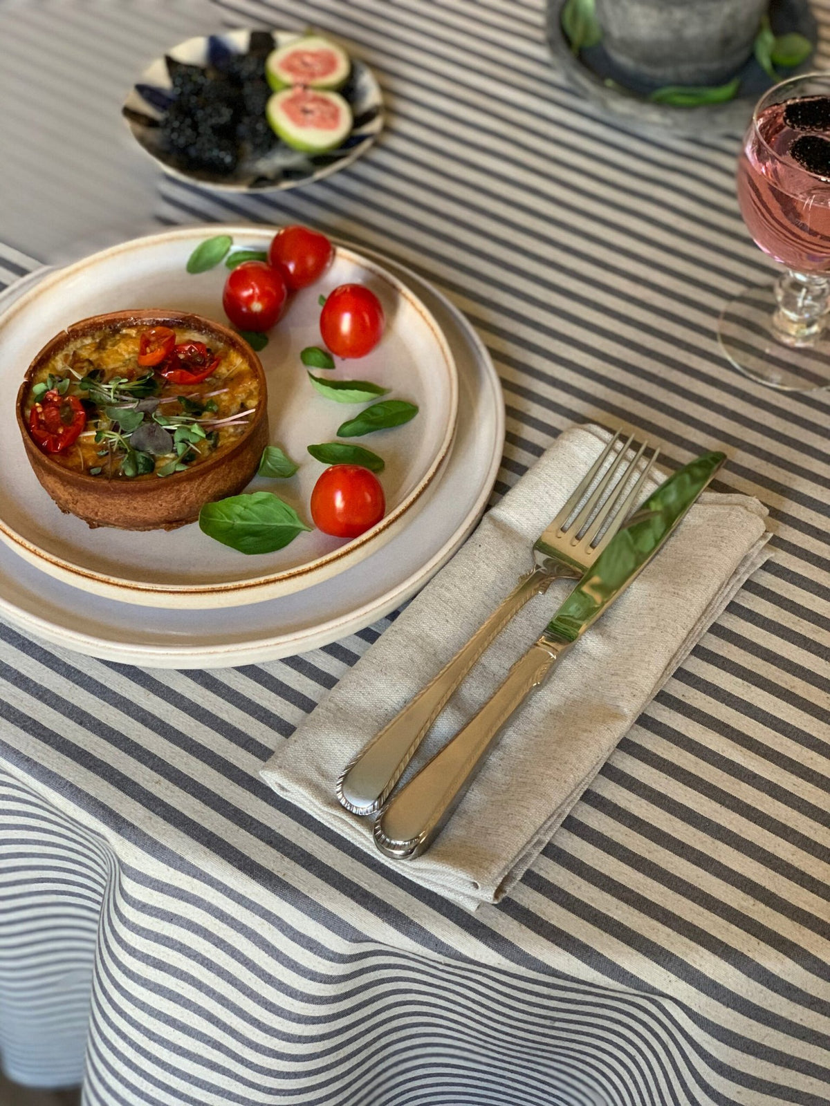2. Close-up of Hortensias Home round tablecloth in beige with blue lines, featuring elegant table setting with quiche and tomatoes