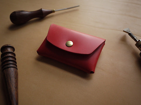 3. Front view of Mirgoods red leather wallet with brass button, surrounded by crafting tools