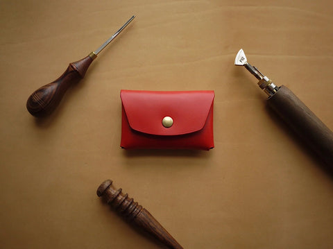 1. Handmade red leather wallet by Mirgoods with brass button, shown with crafting tools