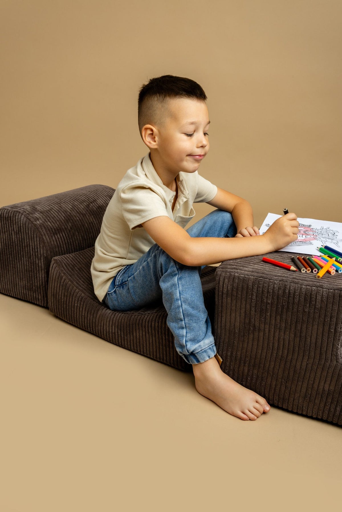 3. Boy drawing on brown velvet corduroy play set with crayons and coloring book on beige background