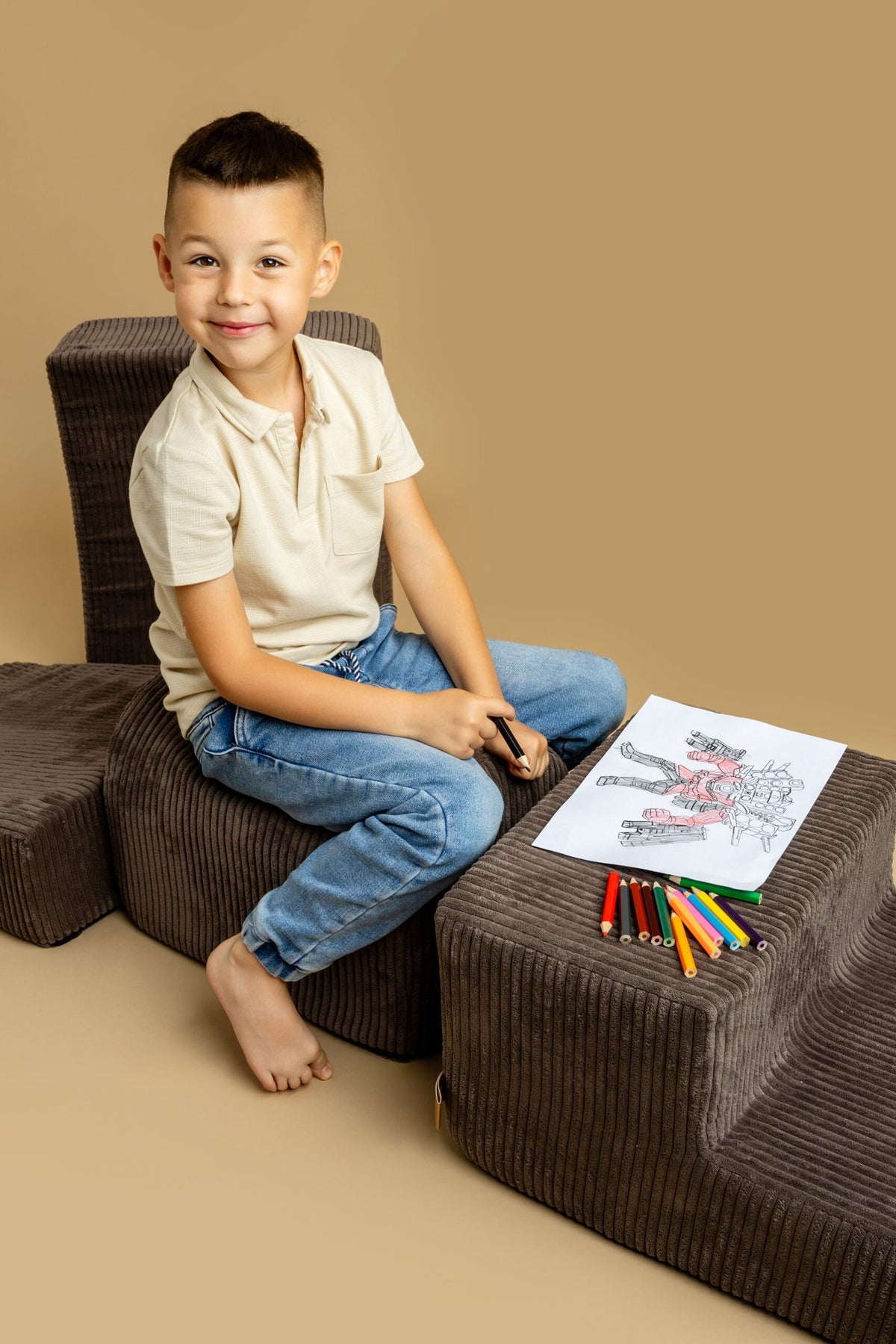 1. Boy sitting on brown velvet corduroy play set with drawing materials on beige background