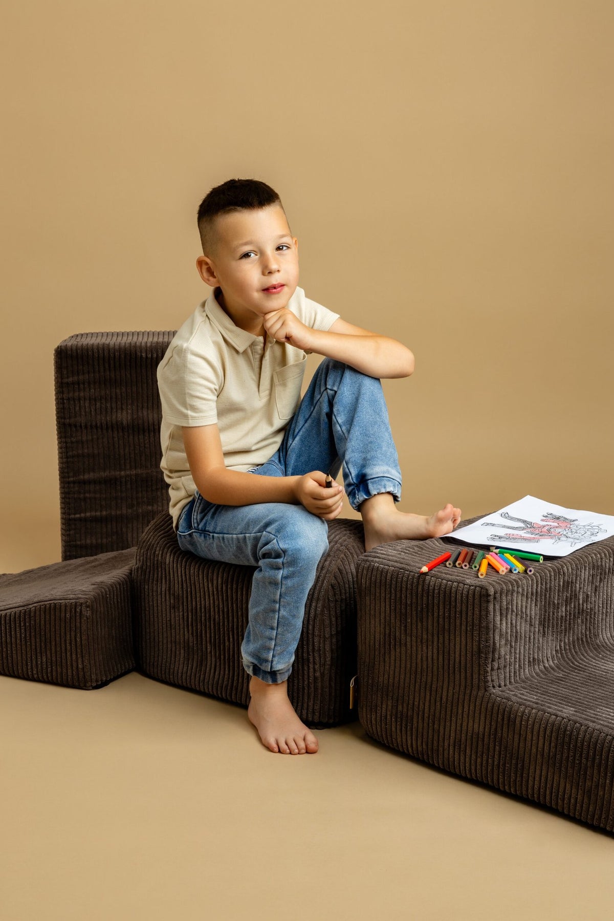 1. Boy sitting on brown velvet corduroy play set with coloring book and crayons on beige background