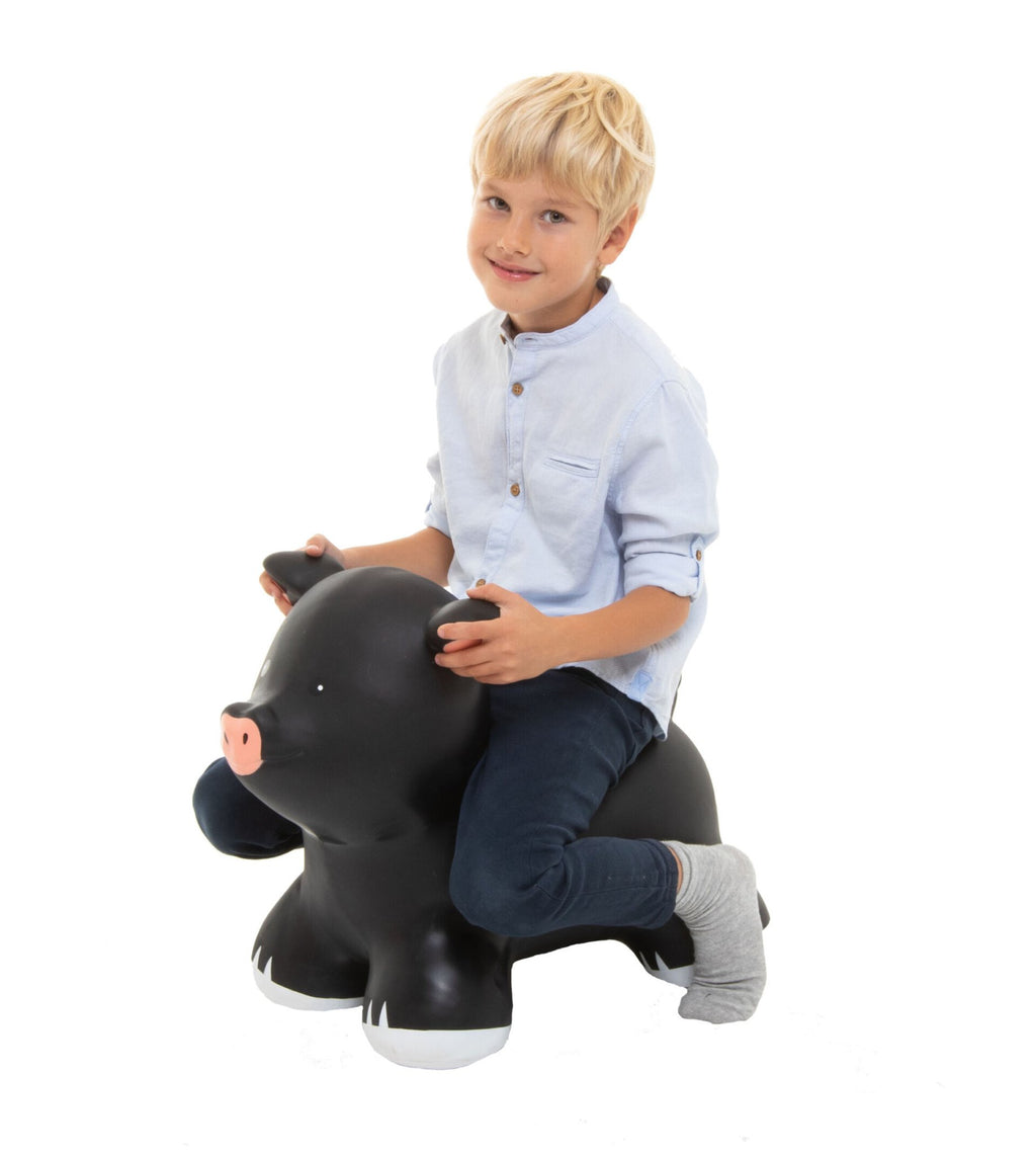 1. Child sitting on black pig-shaped hopper toy wearing light blue shirt and jeans on white background