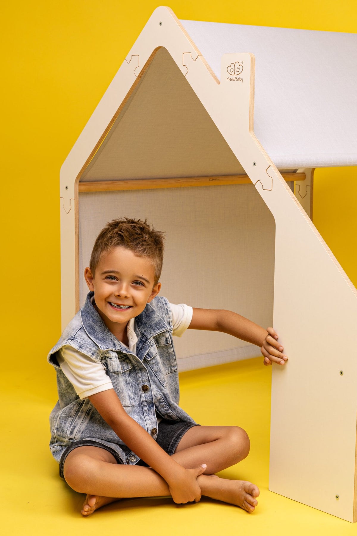 4. Smiling child sitting inside MeowBaby white wooden house with blue roof on yellow background