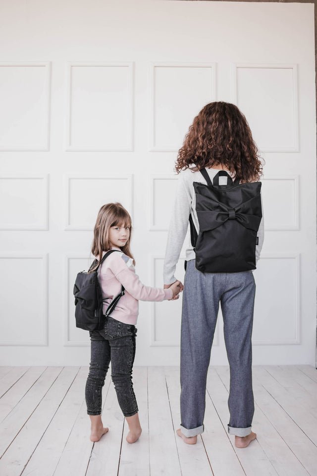 2. Woman and child holding hands, both wearing Muni Black Bow Large waterproof backpacks, highlighting versatility