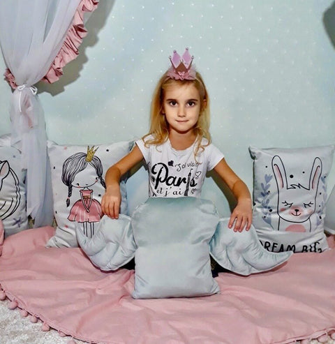 2. Young girl with crown holding grey wing-shaped cushion in a decorated children's room
