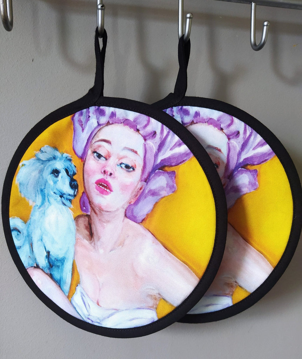 5. Two pot holders with pop art design hanging on hooks, featuring woman and dog illustration