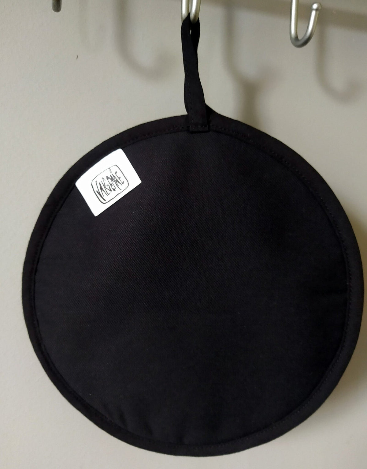 2. Black side of pot holder with Katrin Valgemäe logo, hanging on hooks