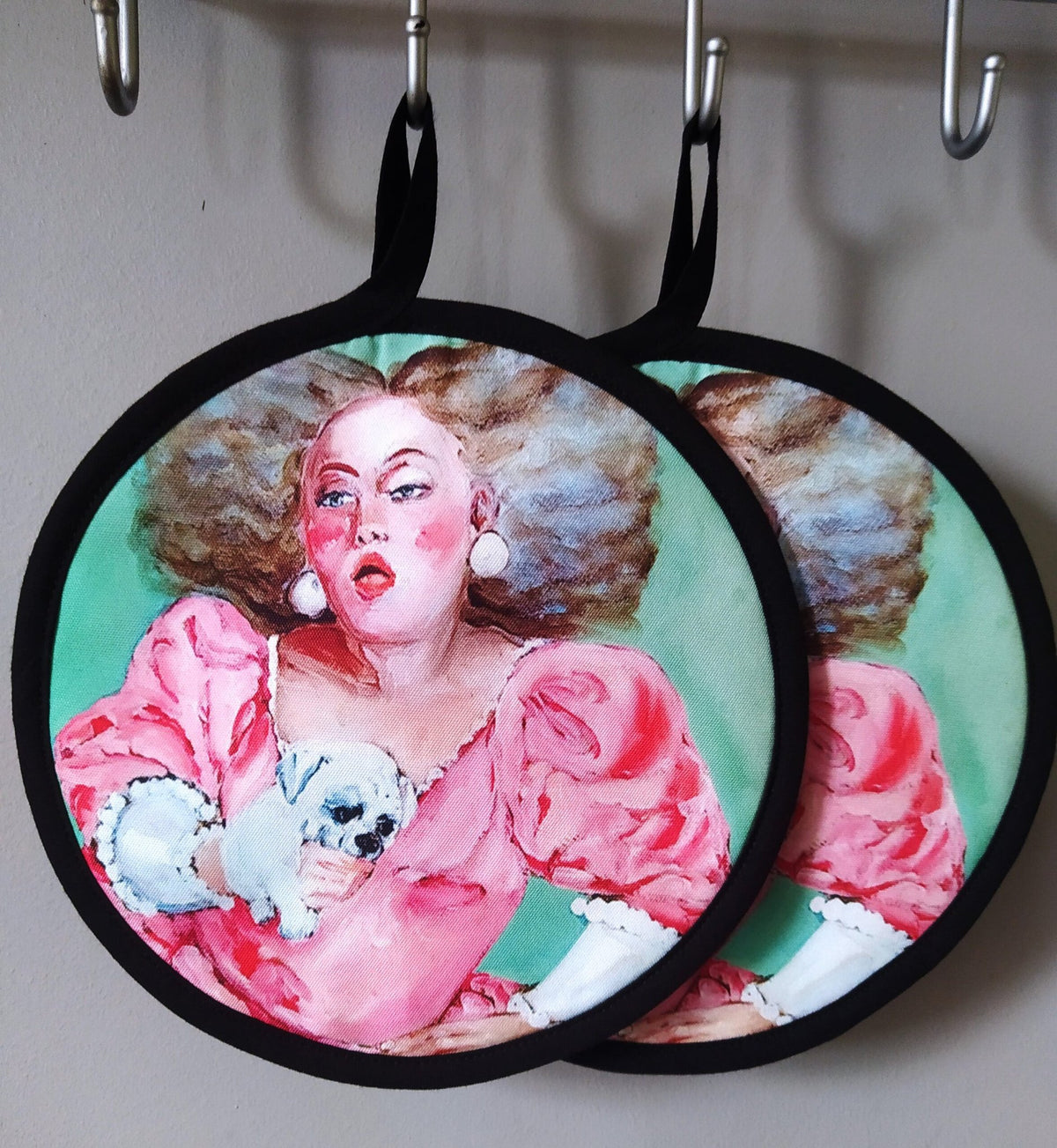 3. Two pot holders with pink dress woman and dog design hanging on hooks