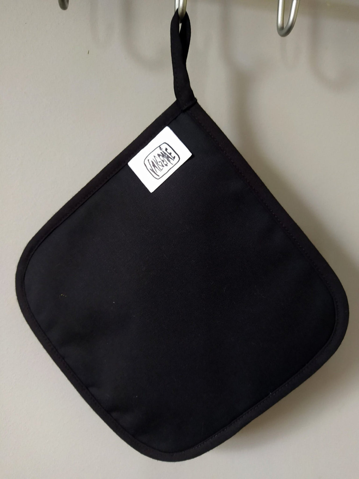 2. Black pot holder with Katrin Valgemäe logo tag hanging on a hook