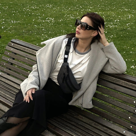 1. Woman sitting on a bench wearing a Drinbags Classic Waist Bag in black, styled with a casual outfit