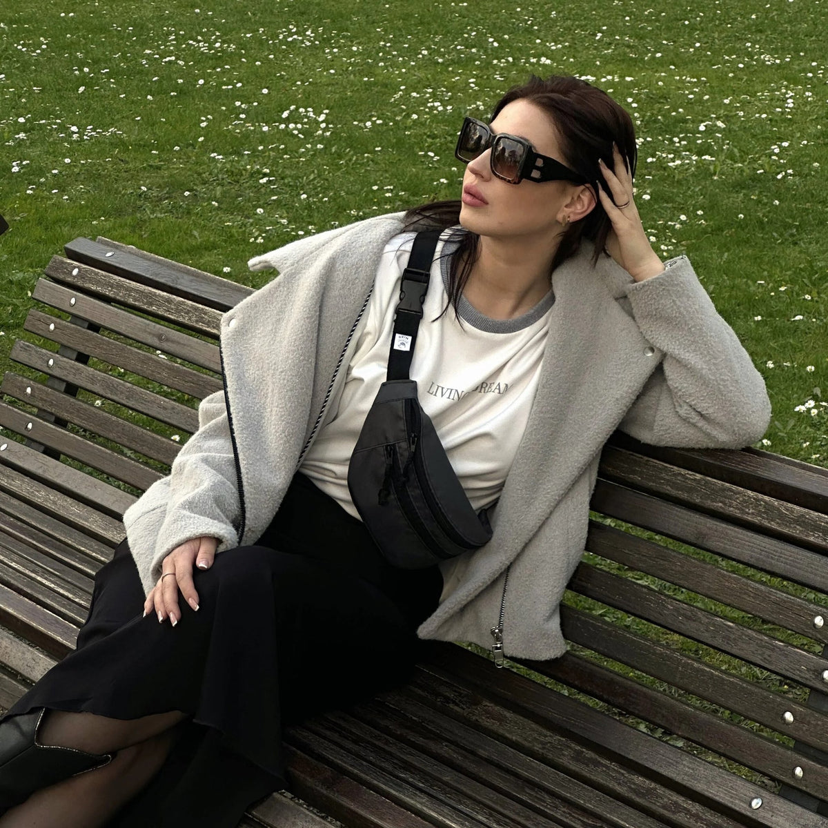 1. Woman wearing Drinbags Classic Grey Waist Bag on a park bench, showcasing adjustable strap and stylish design