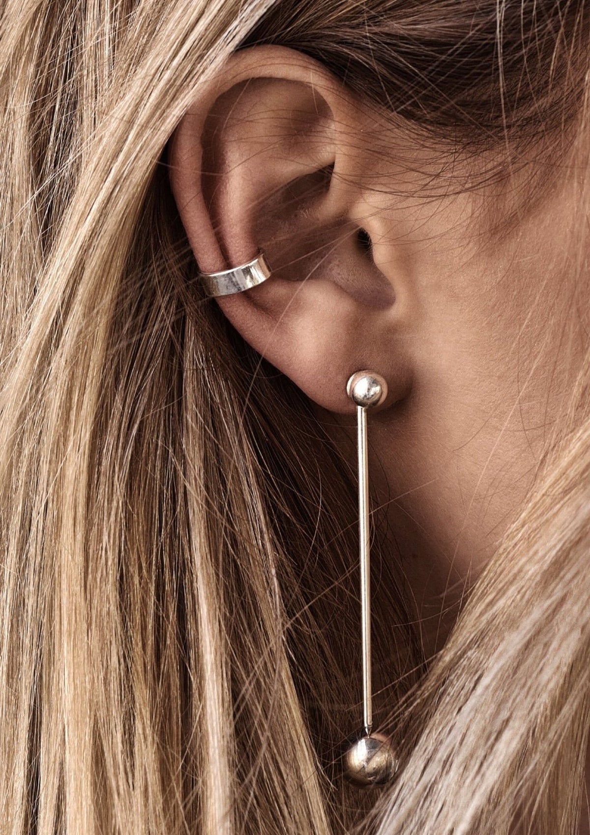 1. Woman wearing NO MORE flat ear cuff in silver, styled with a long drop earring, showcasing chic and effortless elegance