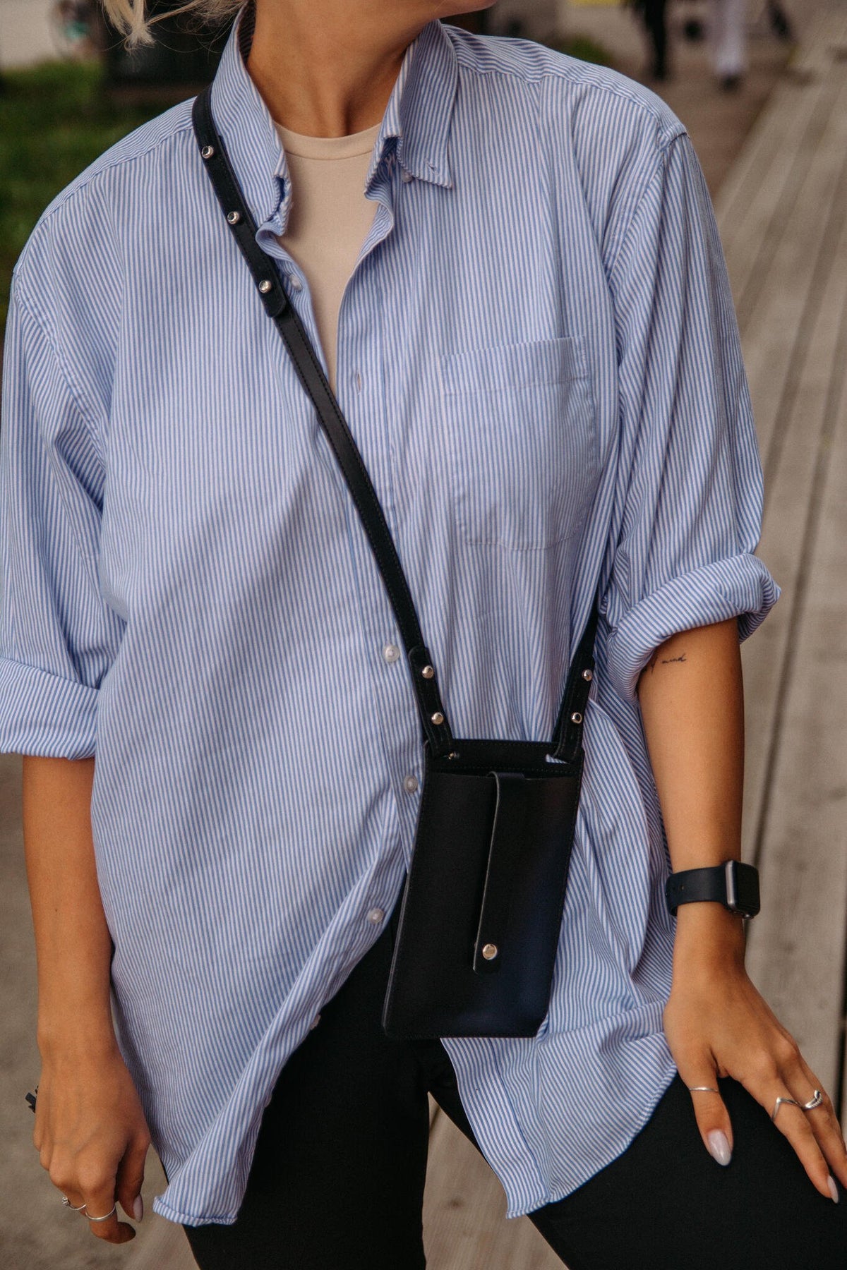 1. Woman wearing black Stella Soomlais By Your Side phone bag with detachable strap over blue striped shirt