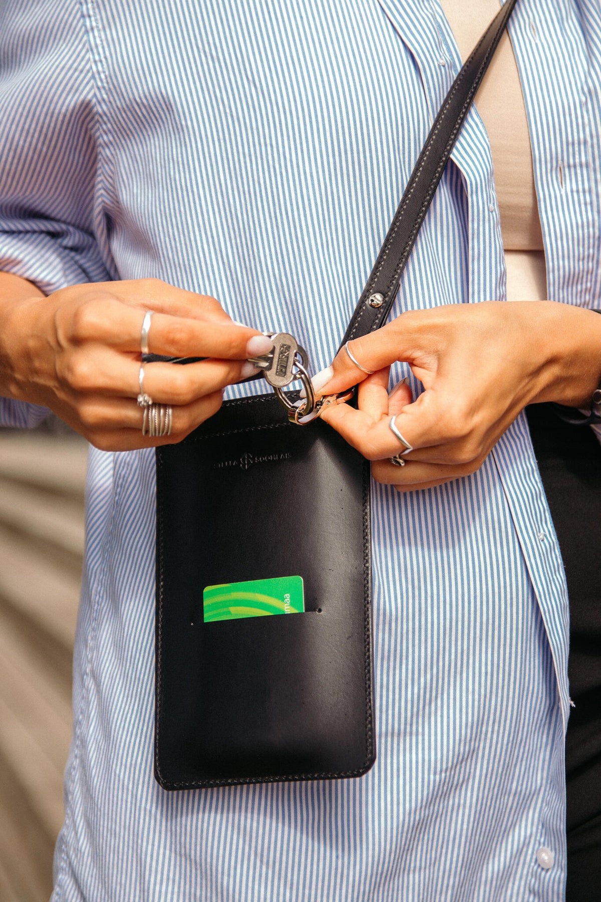 5. Woman holding keys and card with black Stella Soomlais phone bag over blue striped shirt