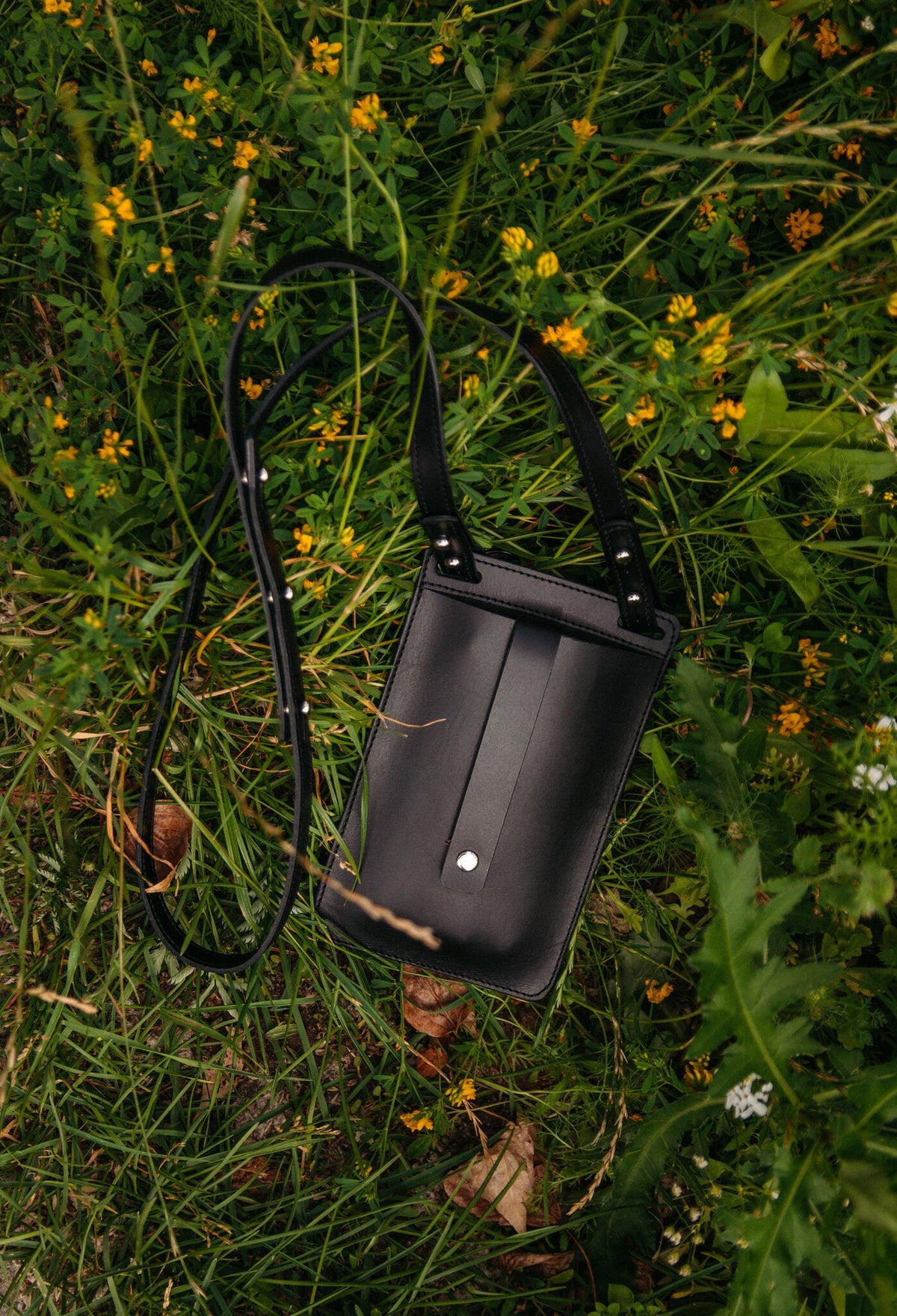 6. Back view of black Stella Soomlais By Your Side phone bag with strap in grassy field