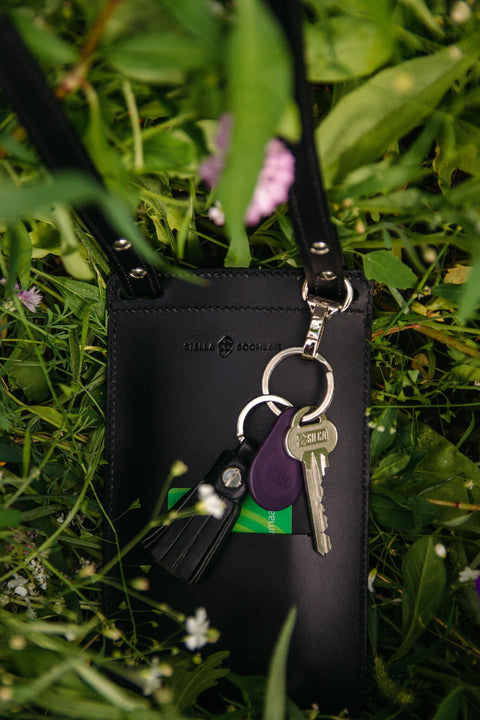 3. Close-up of black Stella Soomlais phone bag with keys and card in pocket among green foliage