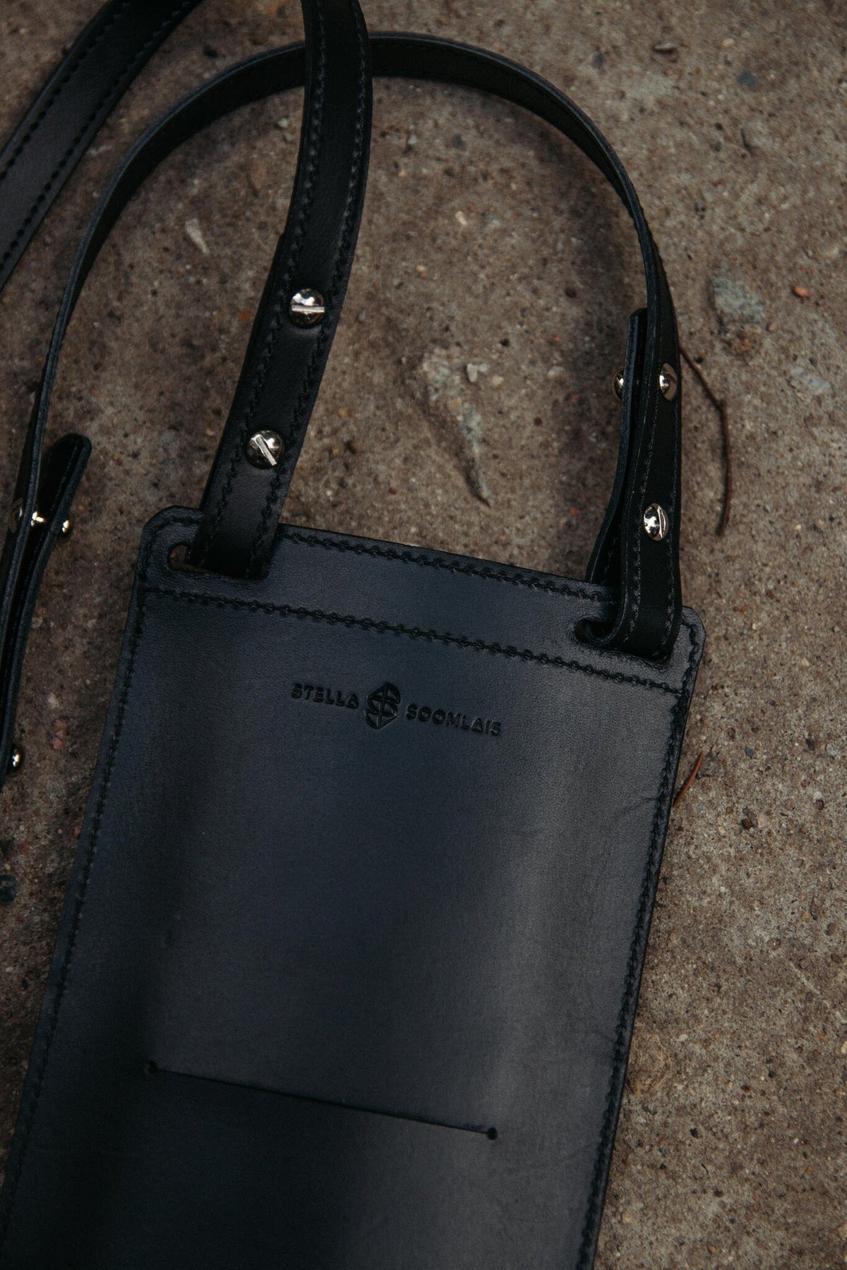 9. Close-up of black Stella Soomlais phone bag showing logo and strap details on concrete