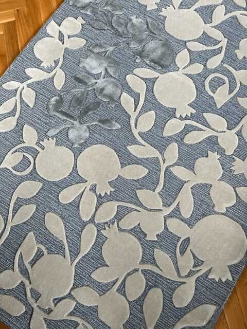 1. Hand-tufted wool rug with pomegranate branch design in beige and grey on a textured blue background
