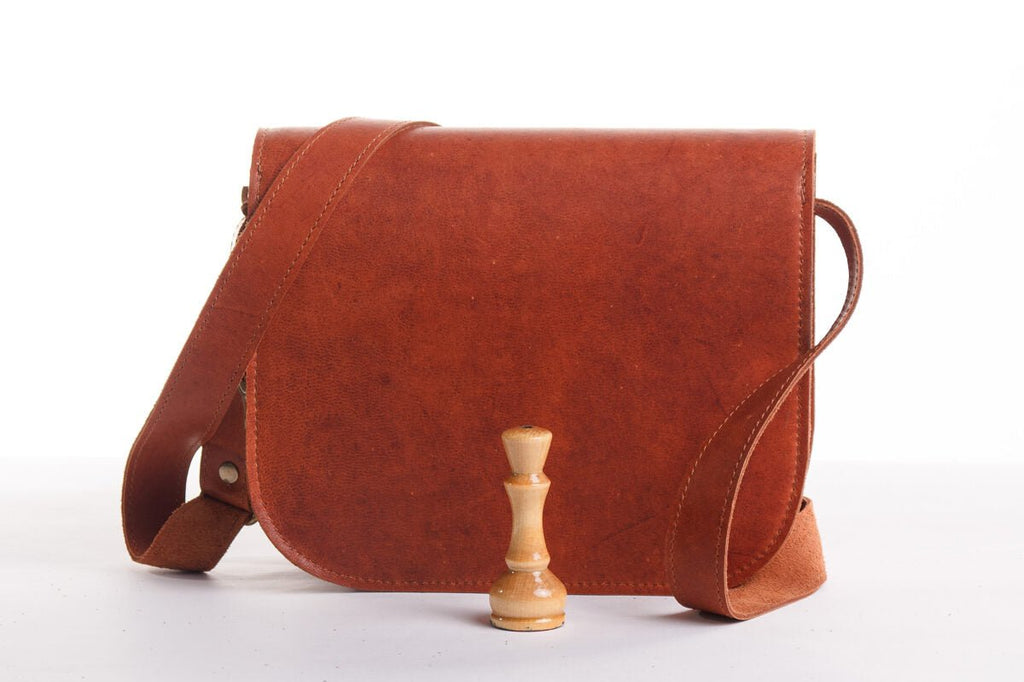 4. Front view of Zelma Kraft natural leather saddle bag in light brown, studio setting with buckle closure