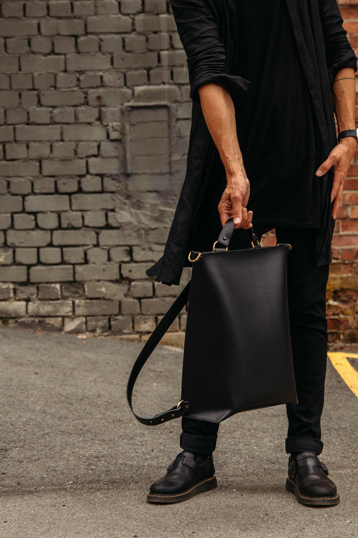 1. Man holding black leather Stella Soomlais backpack by top handle in urban setting