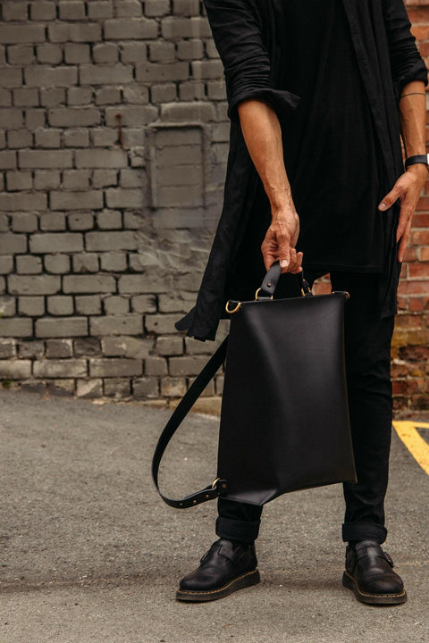 1. Man holding black leather Stella Soomlais backpack by top handle in urban setting
