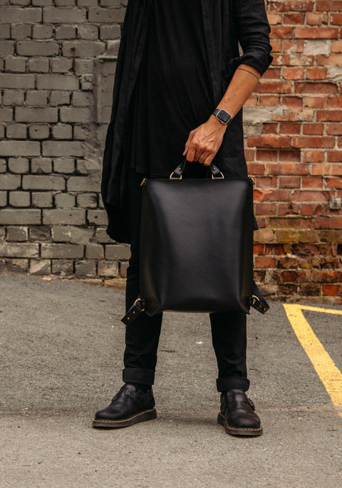 1. Man holding black leather Stella Soomlais backpack by handles in front of brick wall