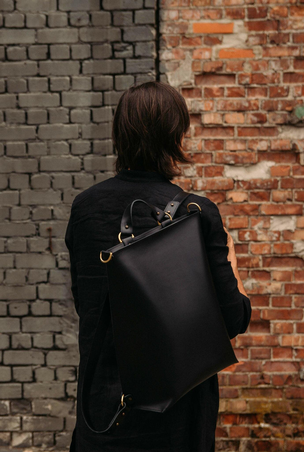 1. Man wearing black leather Stella Soomlais backpack with adjustable straps in front of brick wall