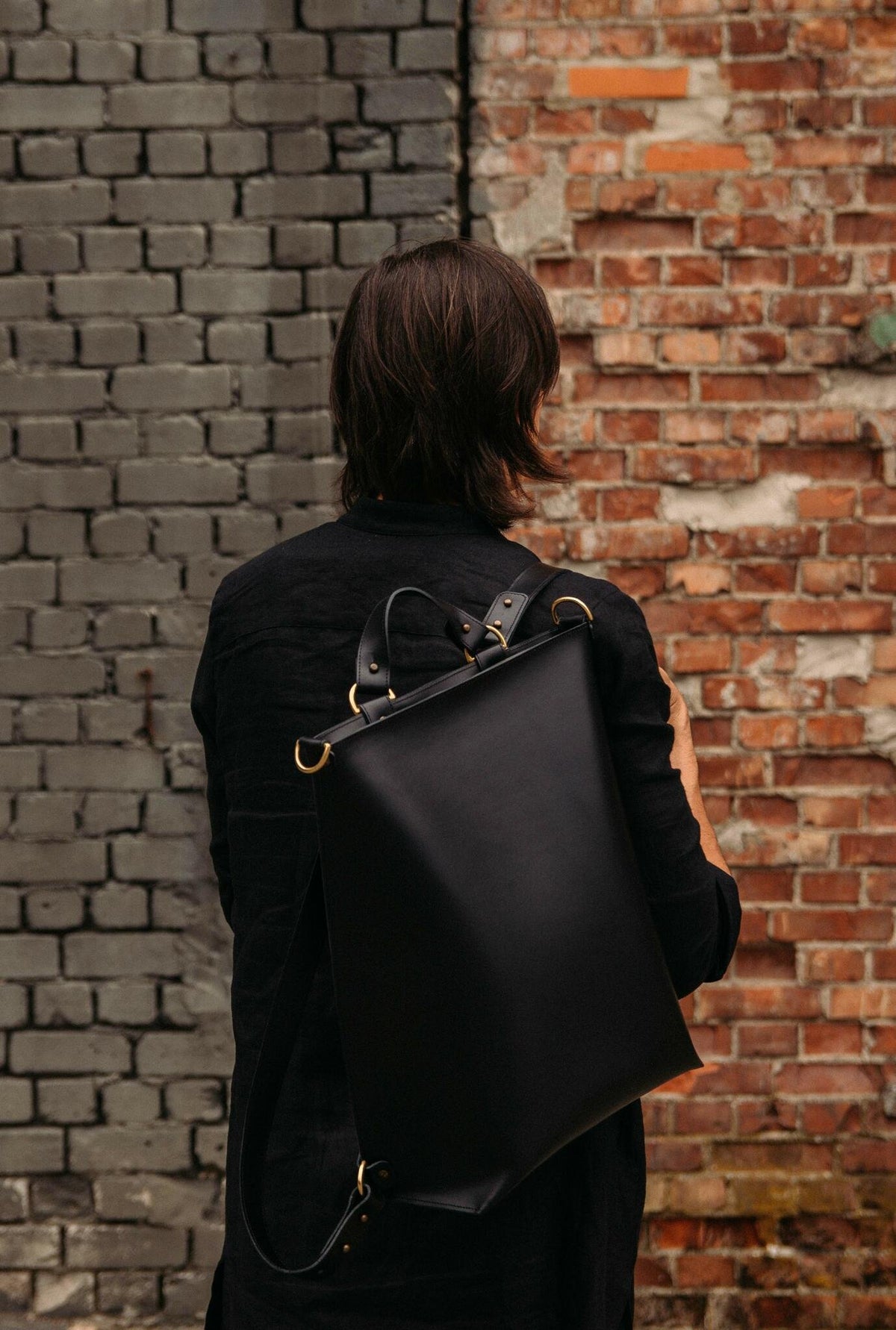 1. Man wearing black leather Stella Soomlais backpack with adjustable straps in front of brick wall
