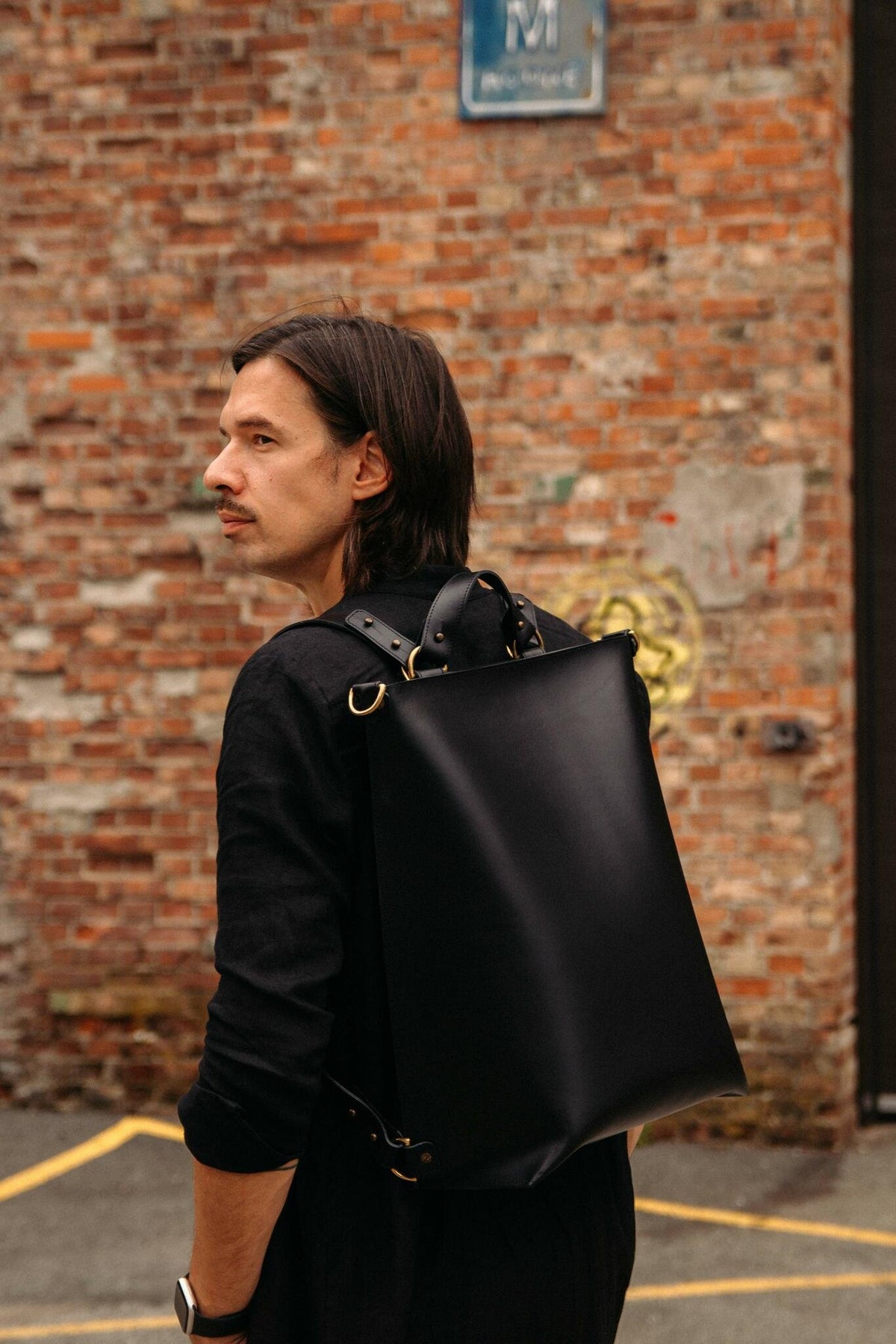 1. Man wearing black leather Stella Soomlais backpack in urban setting with brick wall background