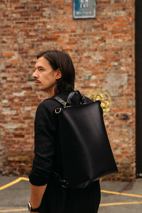 1. Man wearing black leather Stella Soomlais backpack in urban setting with brick wall background