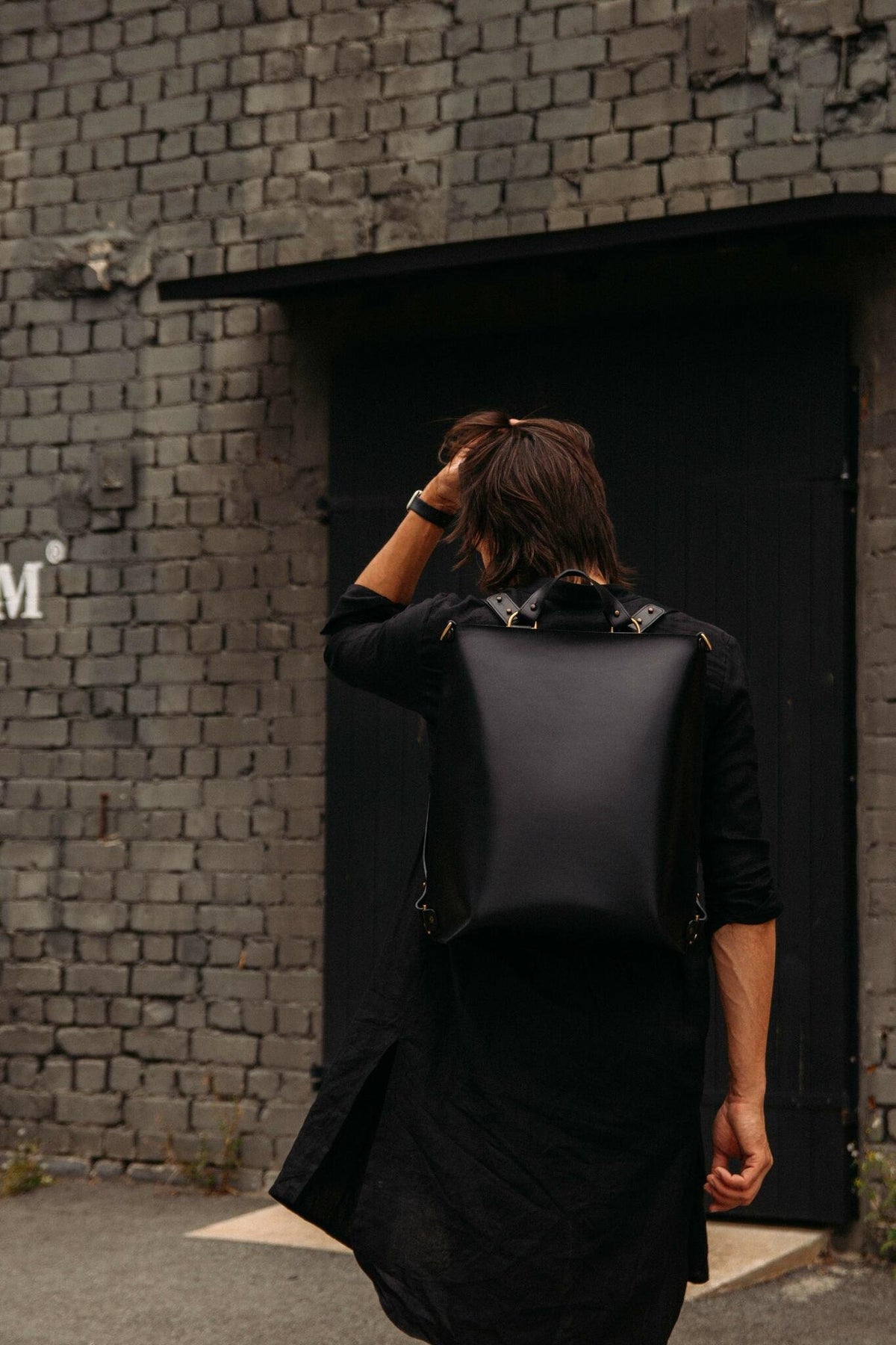 1. Man wearing black leather Stella Soomlais backpack walking away from camera in urban setting