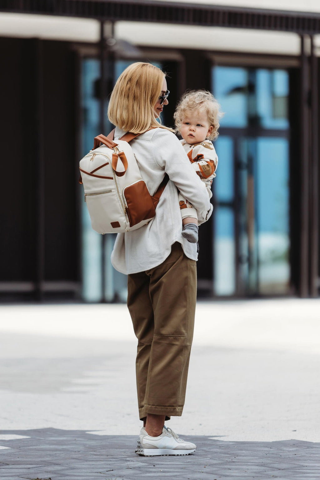 4. Woman holding child with Ally Scandic small cappuccino diaper backpack in city environment