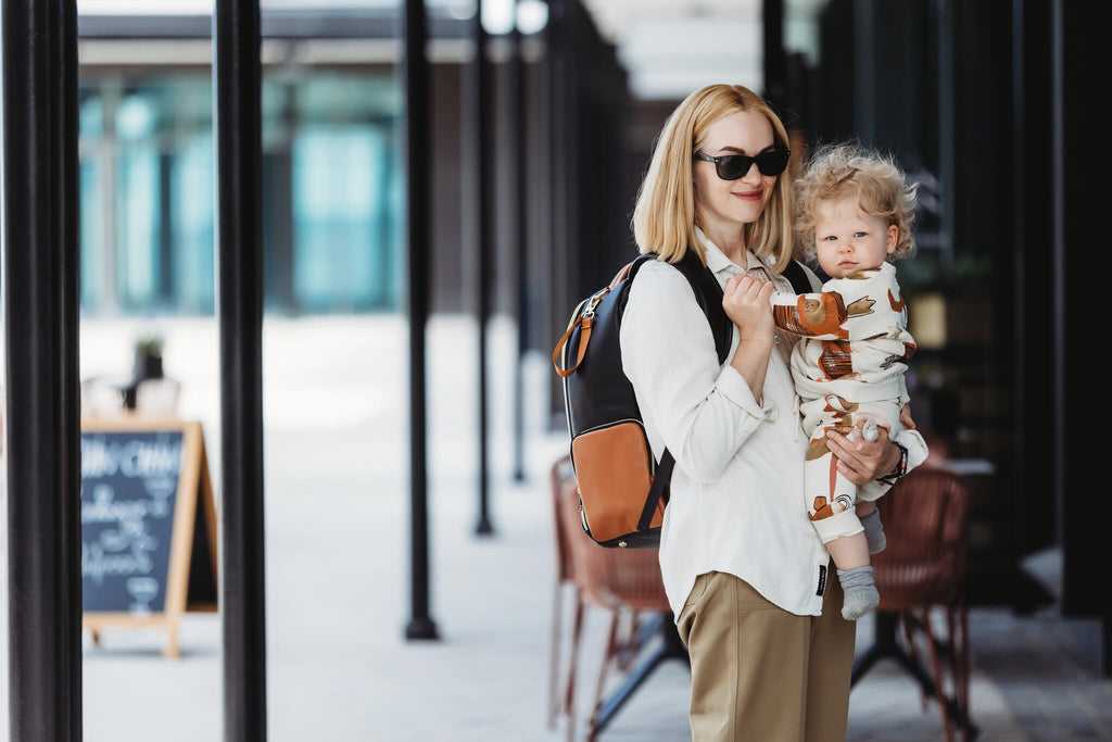 6. Woman holding baby with Ally Scandic Black Coffee diaper backpack in urban setting