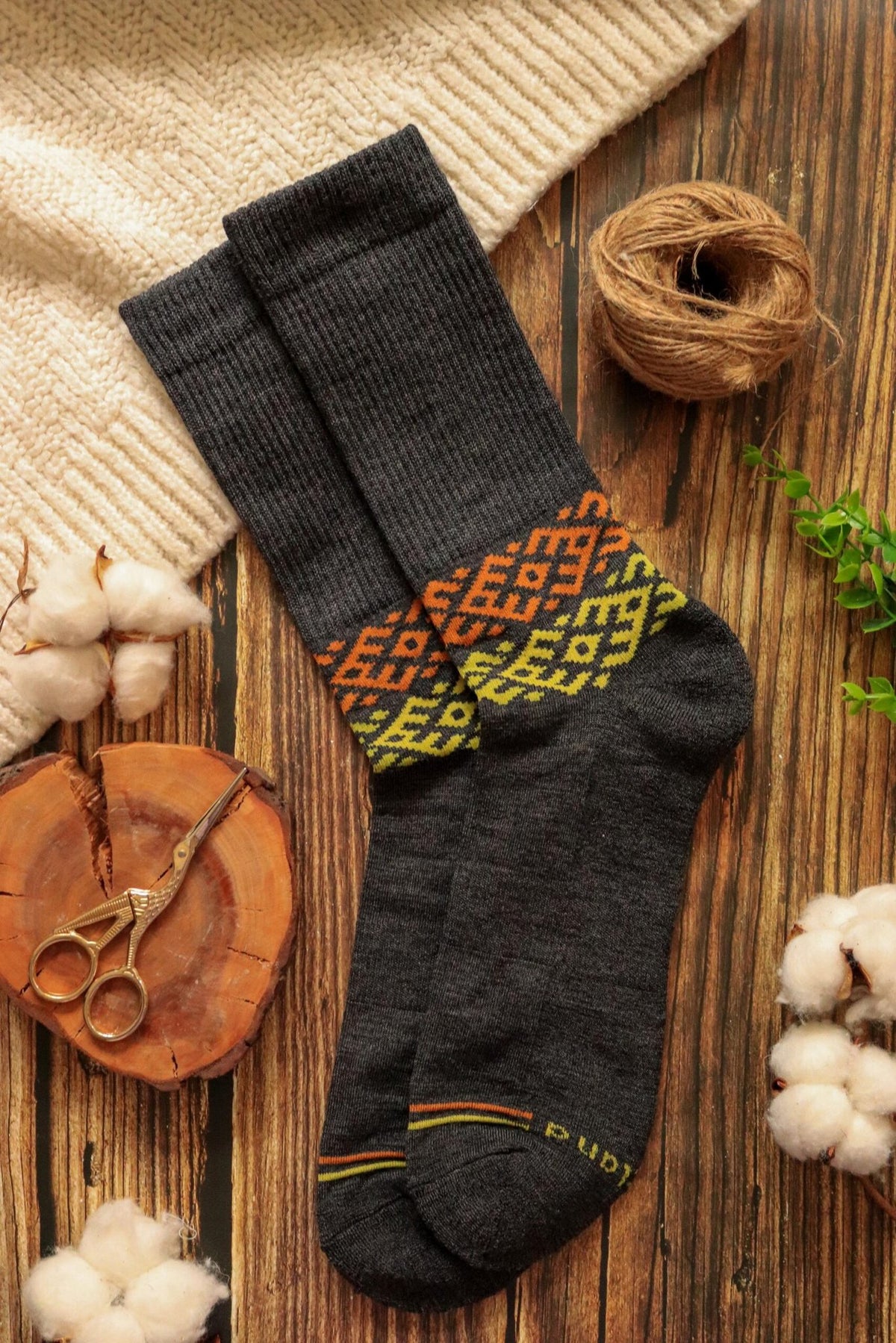 2. Flat lay of Baltland's unisex dark grey merino wool socks with colorful pattern, styled with natural elements