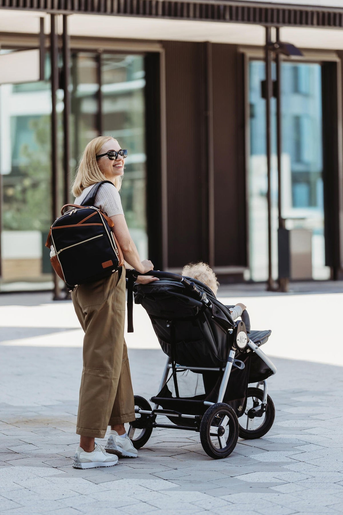 17. Woman pushing stroller with Ally Scandic Small Diaper Backpack in Black Coffee outdoors