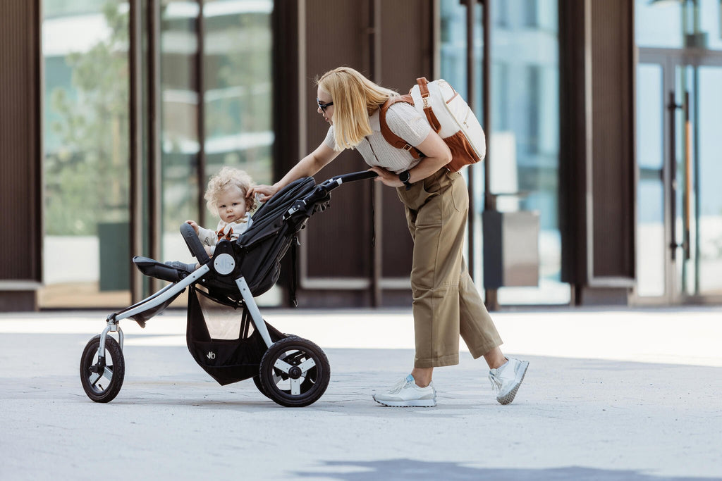 2. Woman pushing stroller with Ally Scandic small cappuccino diaper backpack in urban setting