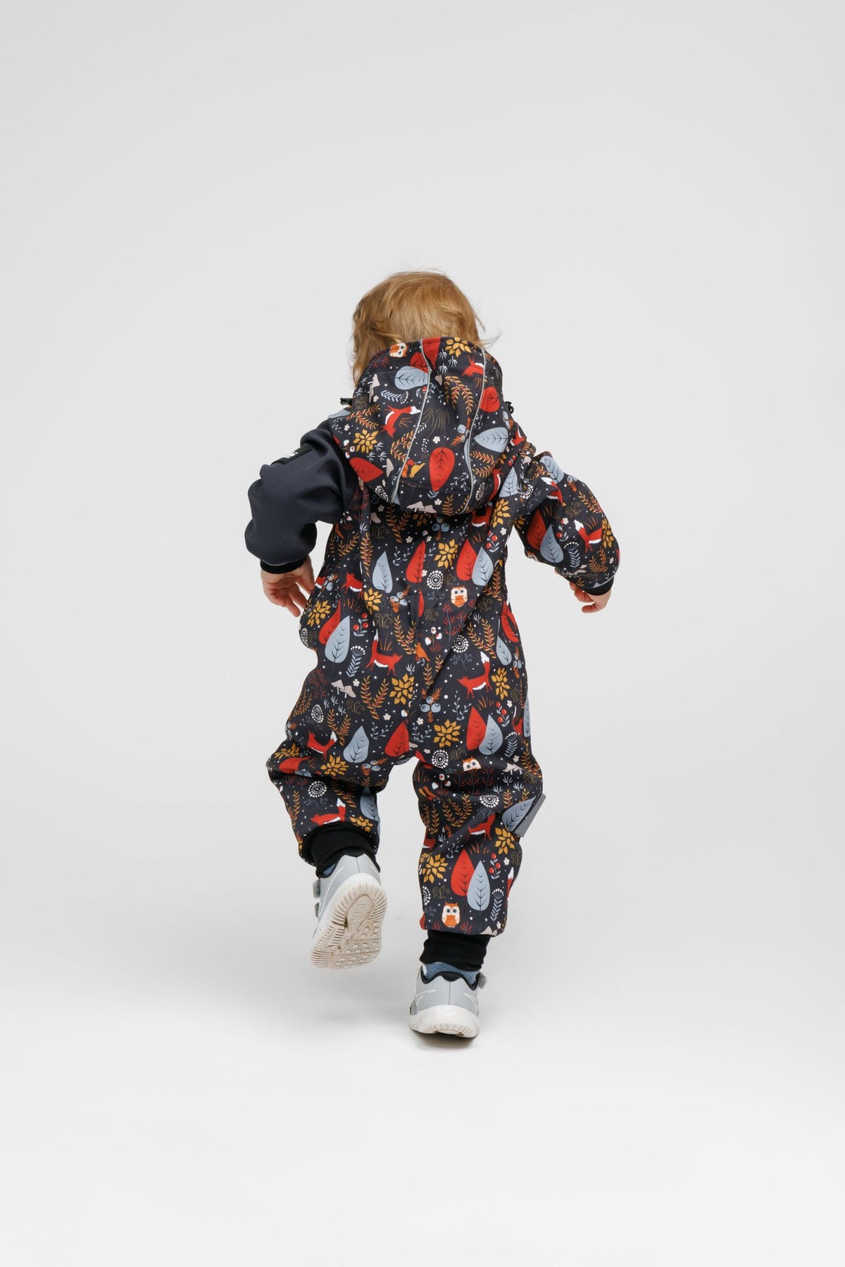 6. Toddler in Nuckö softshell onesie with forest print, shown from back running in studio