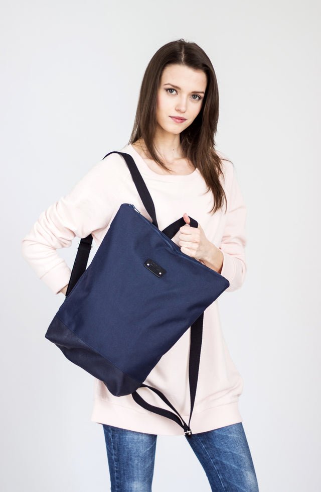 1. Woman holding Muni waterproof backpack with blue leather bottom, styled with casual outfit