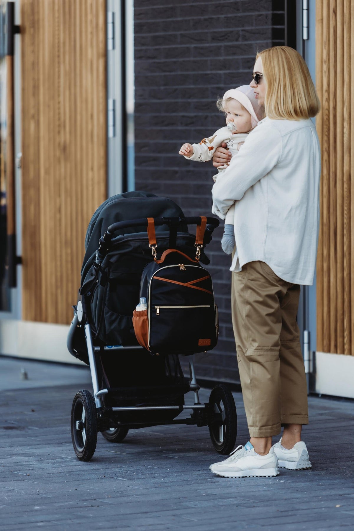 16. Woman with Ally Scandic Small Diaper Backpack in Black Coffee on stroller, holding a child