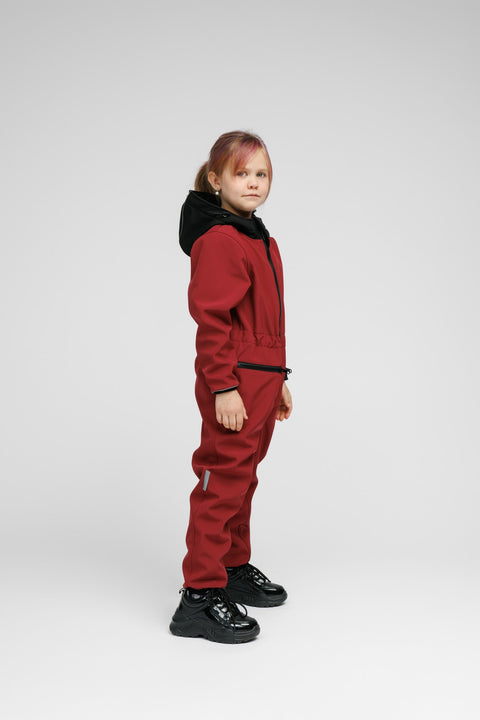 3. Side view of child in Nuckö sunset red softshell onesie with black hood, highlighting adjustable waist and reflective stripe